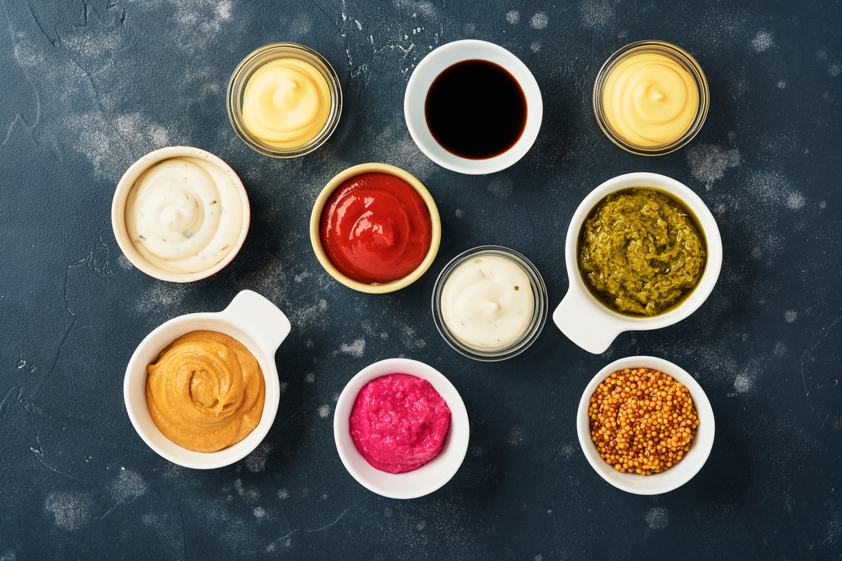 Set of Sauces in Bowls - Ketchup, Mayonnaise, Mustard, Soy Sauce, Bbq Sauce, Pesto, Chimichurri, Mustard Grains on Dark Stone Background. Top View Copy Space
